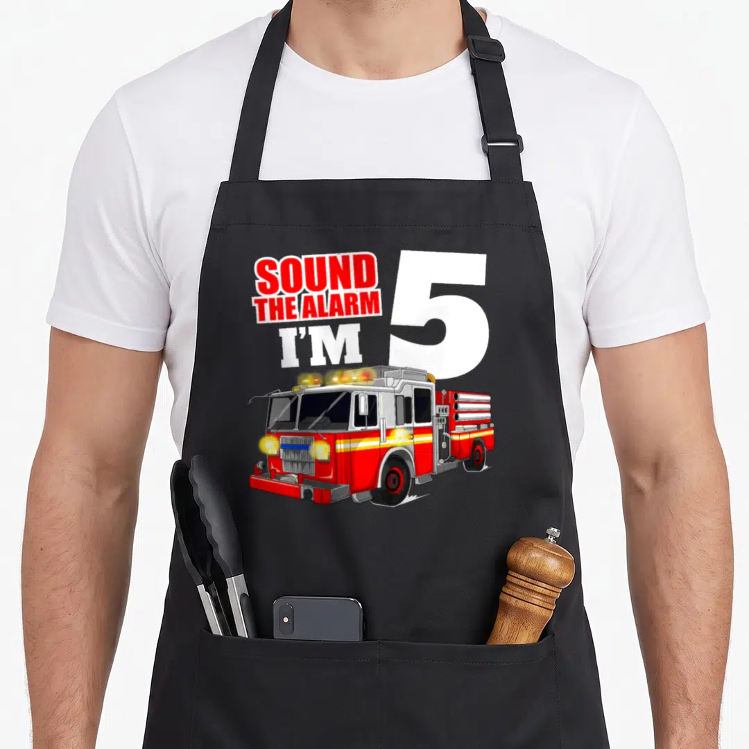 Five truck apron - Cartoon fire truck below Sound The Alarm I'm 5 text — shown on a black cotton canvas apron against a white background