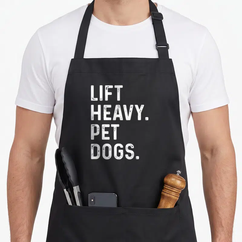 Heavy pet dog apron - White stacked text LIFT HEAVY PET DOGS on black background — shown on a black cotton canvas apron against a white background