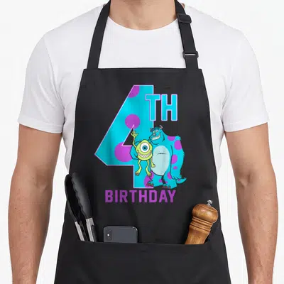 Sully birthday apron - Large number 4 with blue monster and lime green character and BIRTHDAY text — shown on a black cotton canvas apron against a white background