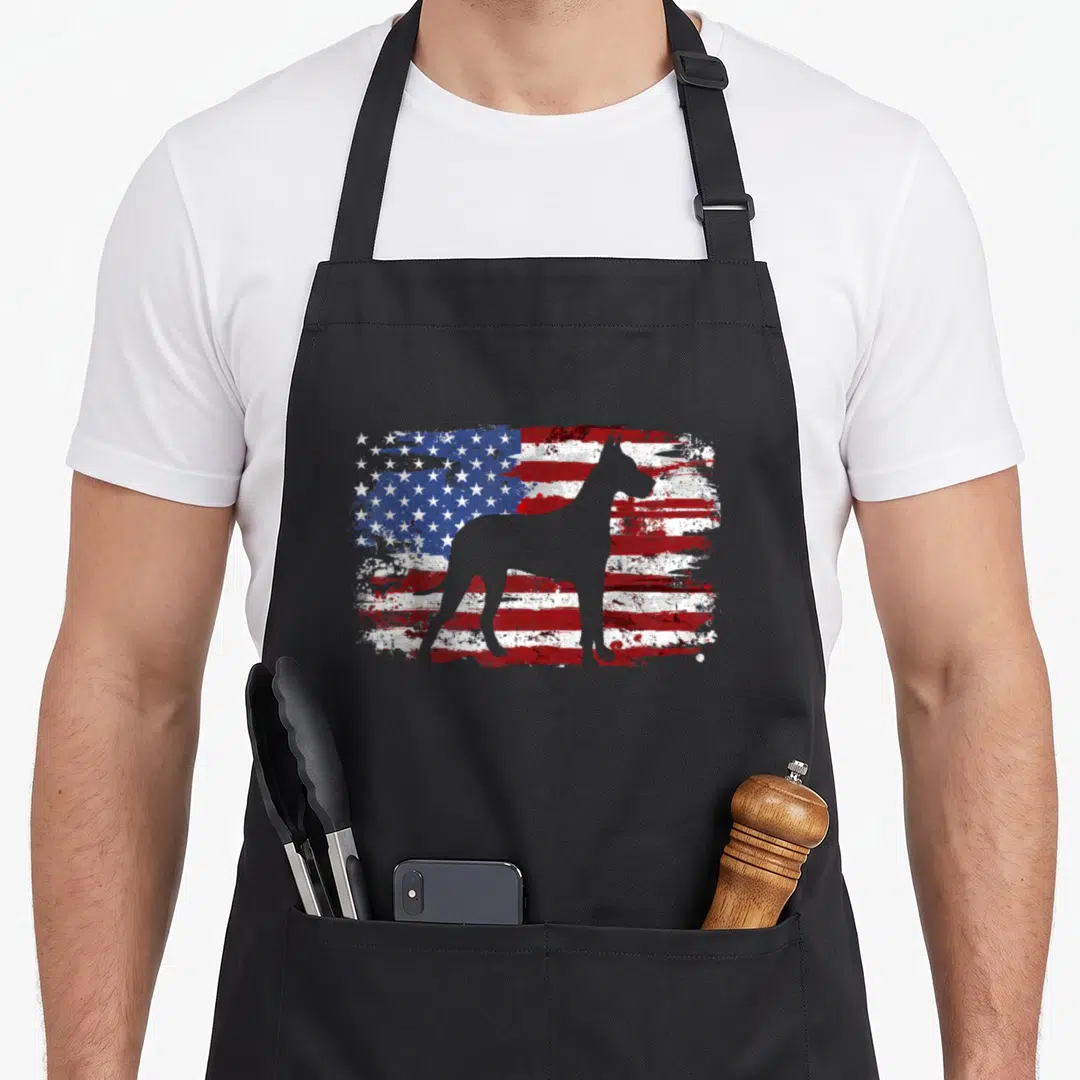 Dane american flag apron - Grey Great Dane silhouette standing before a distressed red white and blue flag — shown on a black cotton canvas apron against a white background