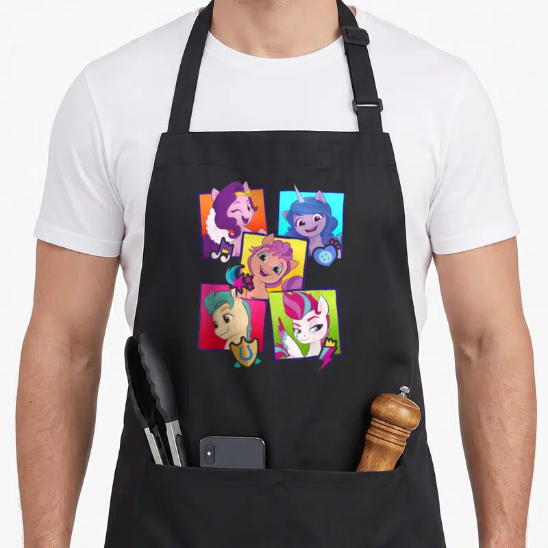 Generation box apron - Four cartoon pony portraits in purple, blue, pink, and yellow squares with scattered button — shown on a black cotton canvas apron against a white background