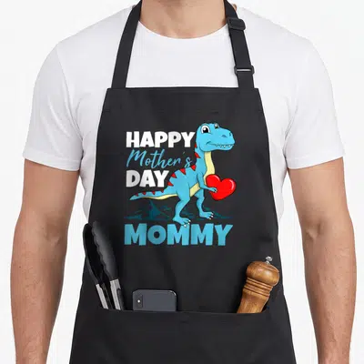 Dino mother's day aprons - Cartoon blue T-Rex holding red heart with HAPPY Mother's DAY MOMMY text and mountain — shown on a black cotton canvas apron against a white background