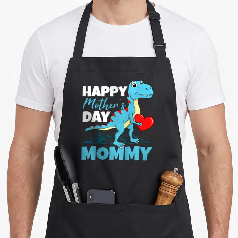 Dino mother's day aprons - Cartoon blue T-Rex holding red heart with HAPPY Mother's DAY MOMMY text and mountain — shown on a black cotton canvas apron against a white background