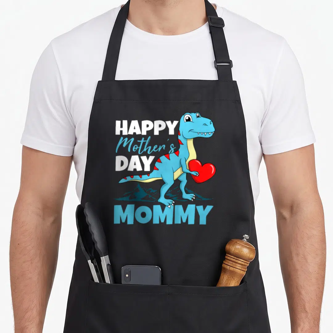 Dino mother's day aprons - Cartoon blue T-Rex holding red heart with HAPPY Mother's DAY MOMMY text and mountain — shown on a black cotton canvas apron against a white background