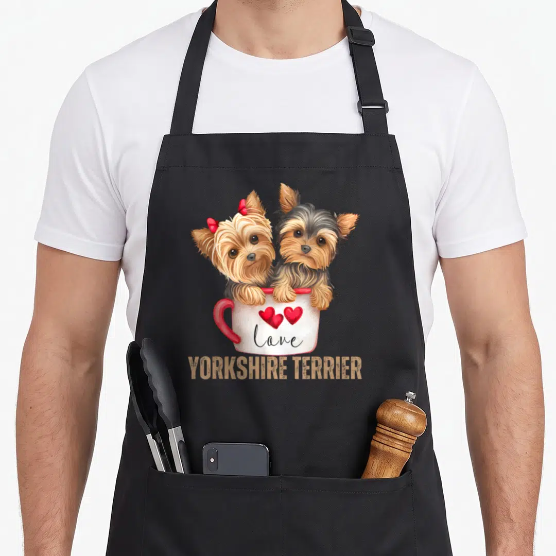 Terrier dog yorkie apron - Two tan and grey Yorkies in a white mug with red hearts and love text — shown on a black cotton canvas apron against a white background