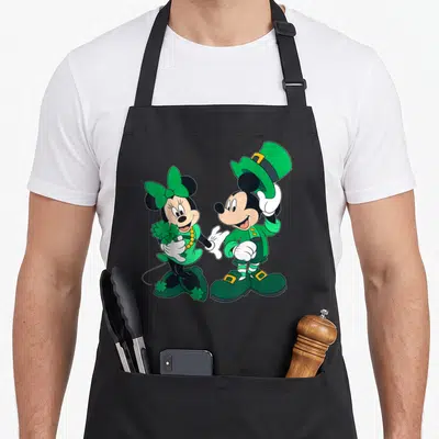 Funny leprechaun st patrick day aprons - Mickey and Minnie in green leprechaun costumes holding clover and tipping hat — shown on a black cotton canvas apron against a white background