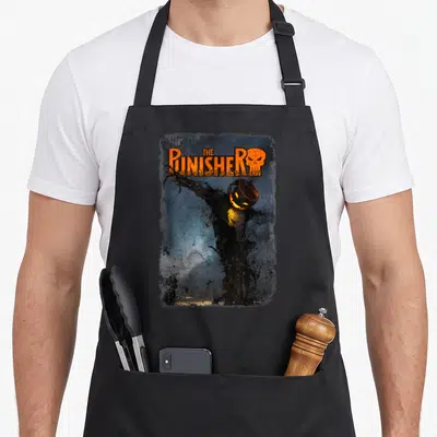 Punisher halloween apron - The Punisher text above pumpkin head scarecrow with skull chest and distressed grey border — shown on a black cotton canvas apron against a white background