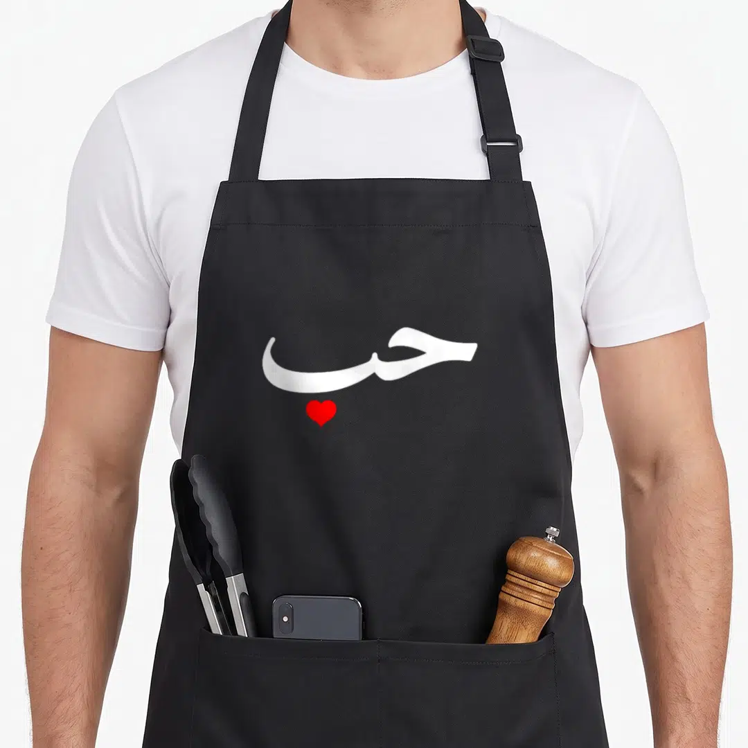 Halal arab apron - White Arabic script positioned above a solid red heart shape — shown on a black cotton canvas apron against a white background