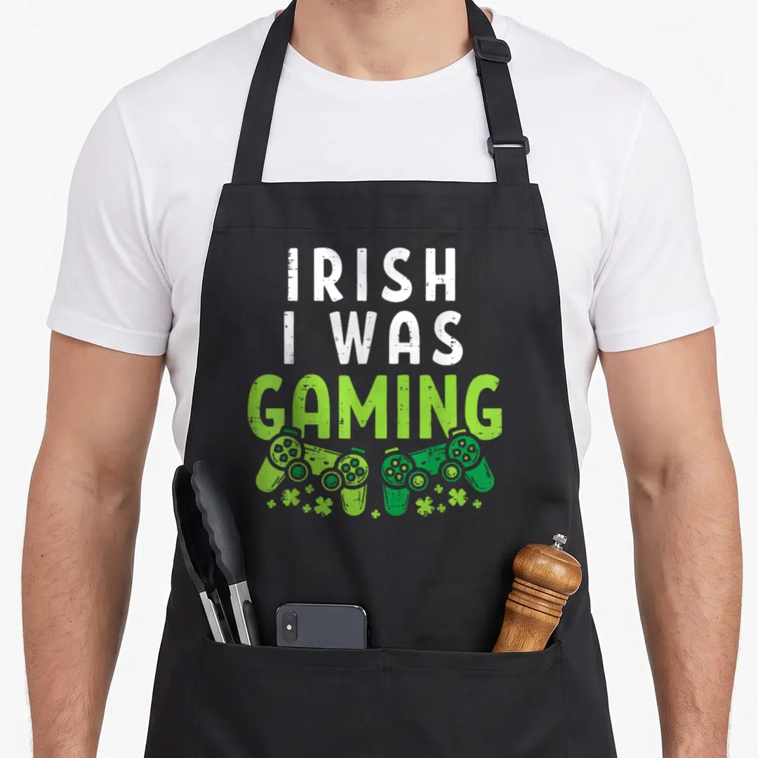 Gaming irish aprons - Stacked IRISH I WAS GAMING text above two green controllers and small shamrocks — shown on a black cotton canvas apron against a white background