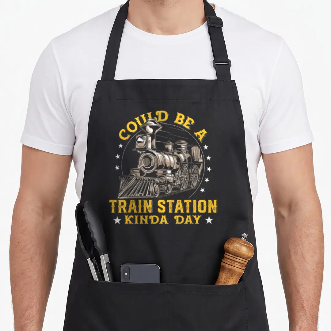 Could railway apron - Yellow Could Be A Train Station Kinda Day text with steam locomotive and white stars on grey — shown on a black cotton canvas apron against a white background