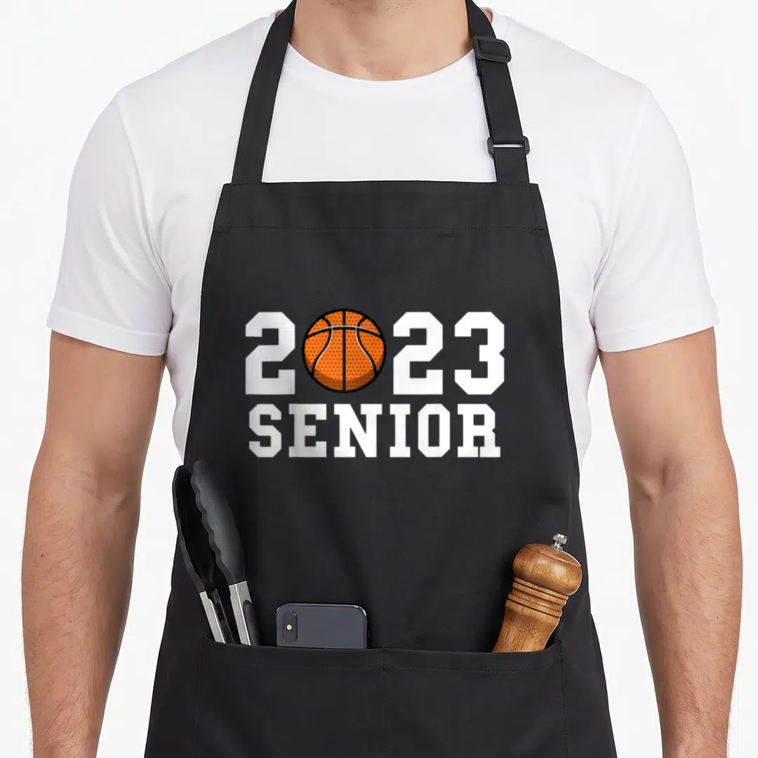 Senior basketball class player apron - 2023 SENIOR text with orange basketball replacing the zero in white and black — shown on a black cotton canvas apron against a white background