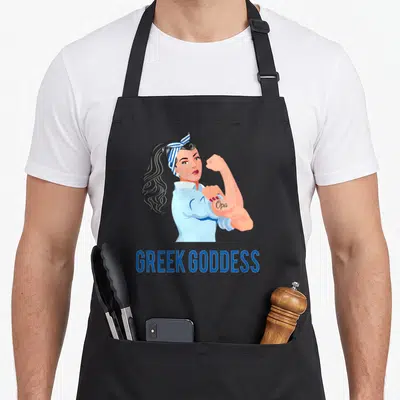 Strong opa greek aprons - Cartoon woman flexing arm with Opa tattoo and GREEK GODDESS text below — shown on a black cotton canvas apron against a white background