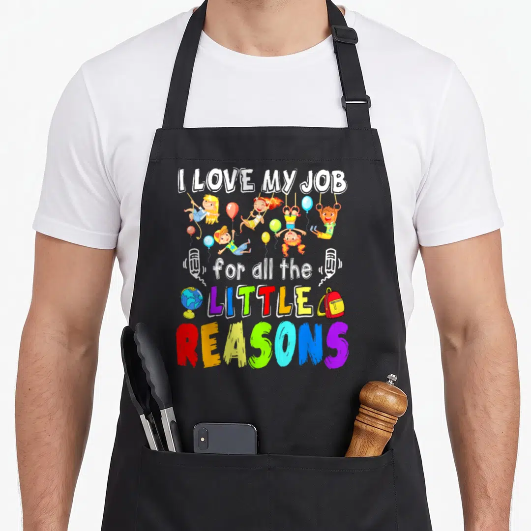 Funny reason apron - Five cartoon children playing with balloons and colorful text reading I Love My Job For All — shown on a black cotton canvas apron against a white background