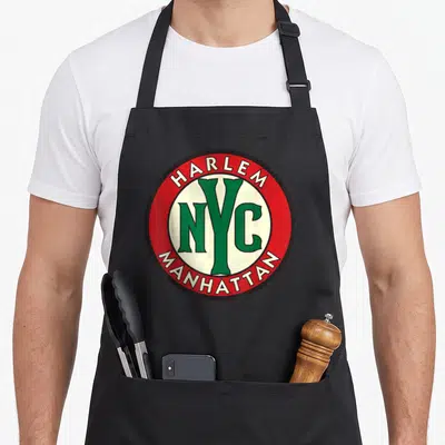 Manhattan nyc apron - Circular red emblem with HARLEM NYC MANHATTAN text in green and white — shown on a black cotton canvas apron against a white background