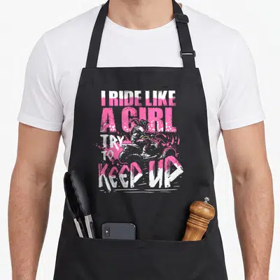 Quad atv girl apron - Pink and white distressed text I RIDE LIKE A GIRL TRY TO KEEP UP with motocross rider graphic — shown on a black cotton canvas apron against a white background