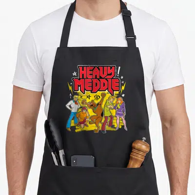 Meddle heavy apron - Stacked red HEAVY MEDDLE! text above five cartoon characters on a yellow splash background — shown on a black cotton canvas apron against a white background
