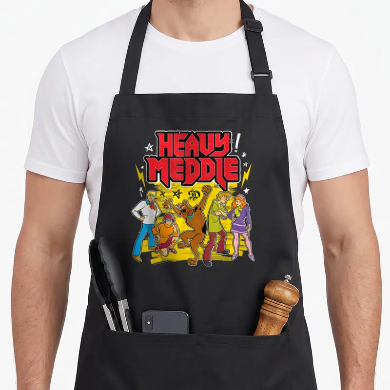 Meddle heavy apron - Stacked red HEAVY MEDDLE! text above five cartoon characters on a yellow splash background — shown on a black cotton canvas apron against a white background