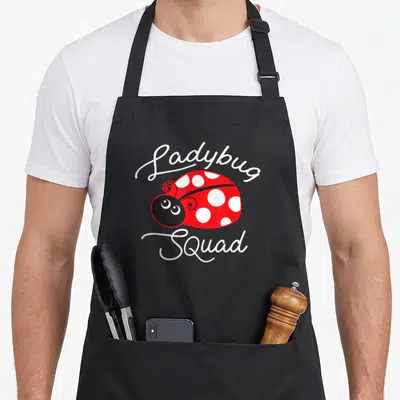 Funny squad ladybug apron - Cartoon red ladybug with white spots centered between white script reading Ladybug Squad — shown on a black cotton canvas apron against a white background
