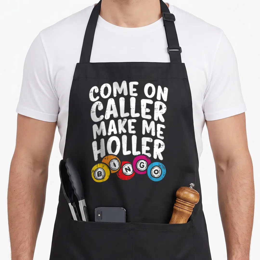 Come bingo apron - White text Come On Caller Make Me Holler above five colorful BINGO chips on black fabric — shown on a black cotton canvas apron against a white background