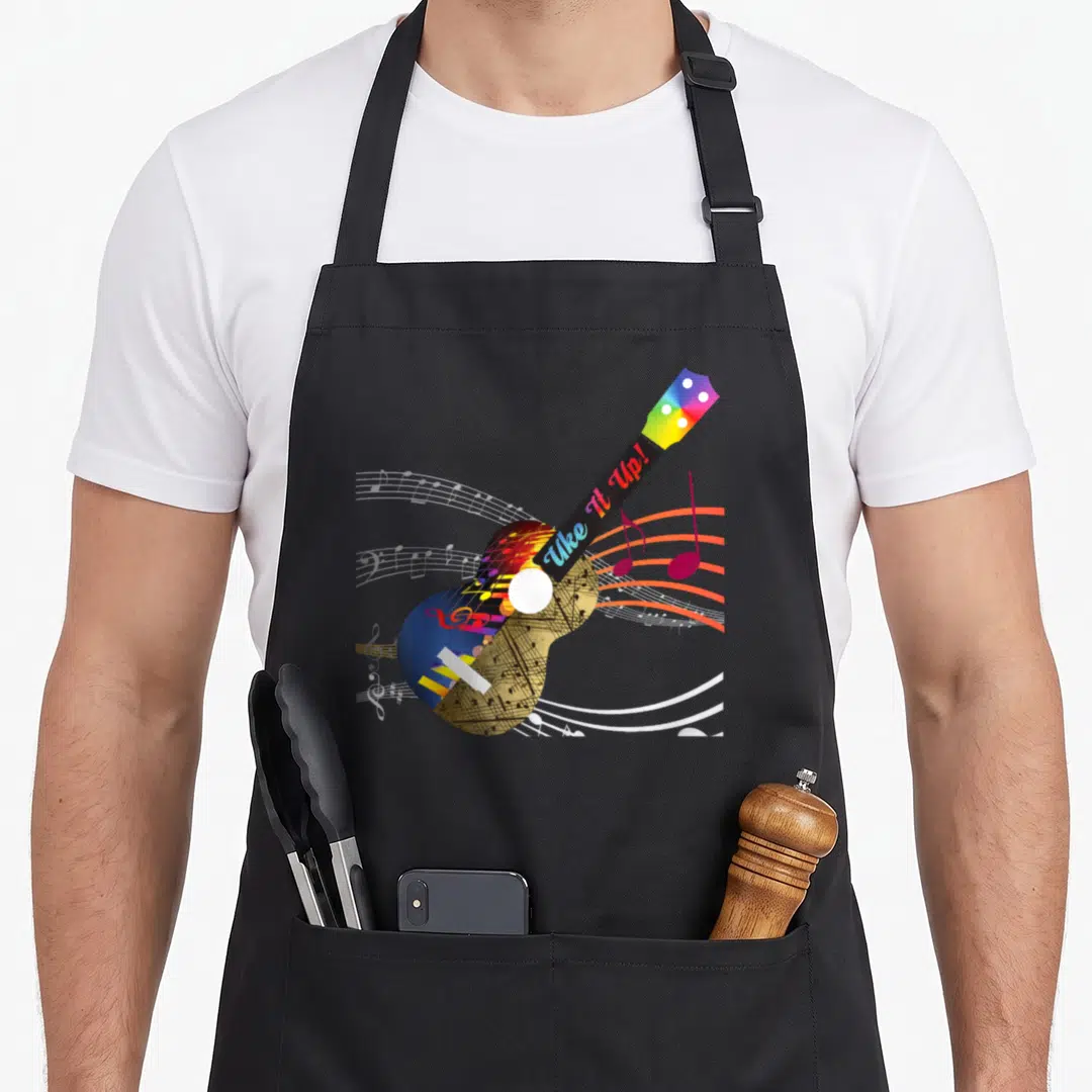 Musical ukulele apron - Colorful ukulele with Uke It Up text and musical notes on staff lines — shown on a black cotton canvas apron against a white background