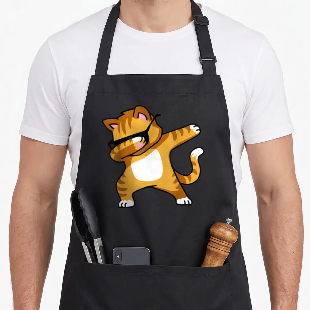 Dab kitty cat apron - Cartoon orange tabby cat wearing black sunglasses performing a dab dance pose — shown on a black cotton canvas apron against a white background