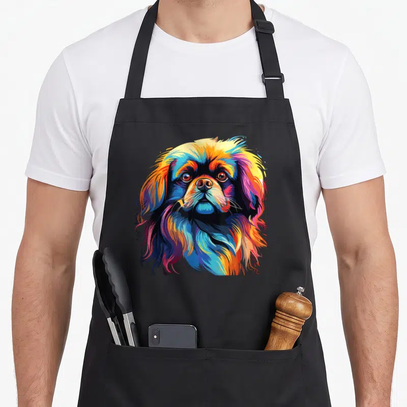 Colorful pekingese dog apron - Realistic multicolored Pekingese dog head print in blue, yellow, red, and orange — shown on a black cotton canvas apron against a white background