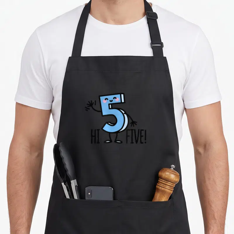 Waving birthday apron - Cartoon blue number 5 with pink cheeks waving above black HI FIVE text — shown on a black cotton canvas apron against a white background