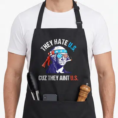 Hate 4th of july apron - George Washington portrait with sunglasses headband and THEY HATE U.S. CUZ THEY AINT U.S. text — shown on a black cotton canvas apron against a white background