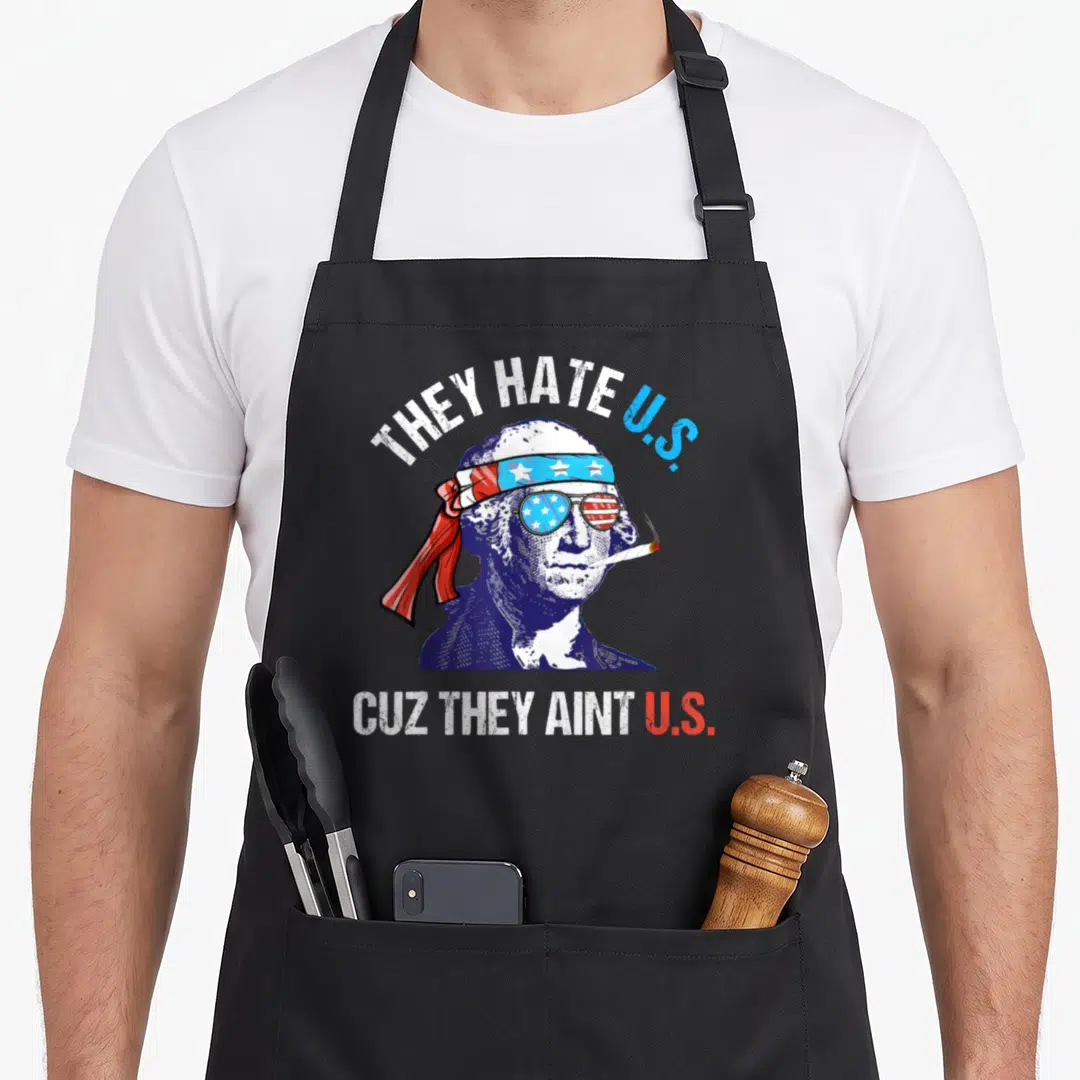 Hate 4th of july apron - George Washington portrait with sunglasses headband and THEY HATE U.S. CUZ THEY AINT U.S. text — shown on a black cotton canvas apron against a white background