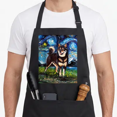 Aja dog apron - Black and tan dog standing on green grass under a swirling blue starry night sky in watercolor style — shown on a black cotton canvas apron against a white background