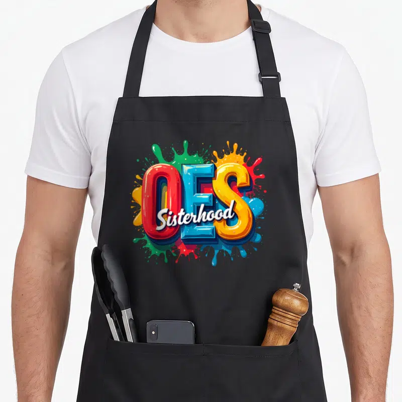 Watercolor oes apron - Large 3D OES letters with Sisterhood script over red blue yellow green paint splashes — shown on a black cotton canvas apron against a white background