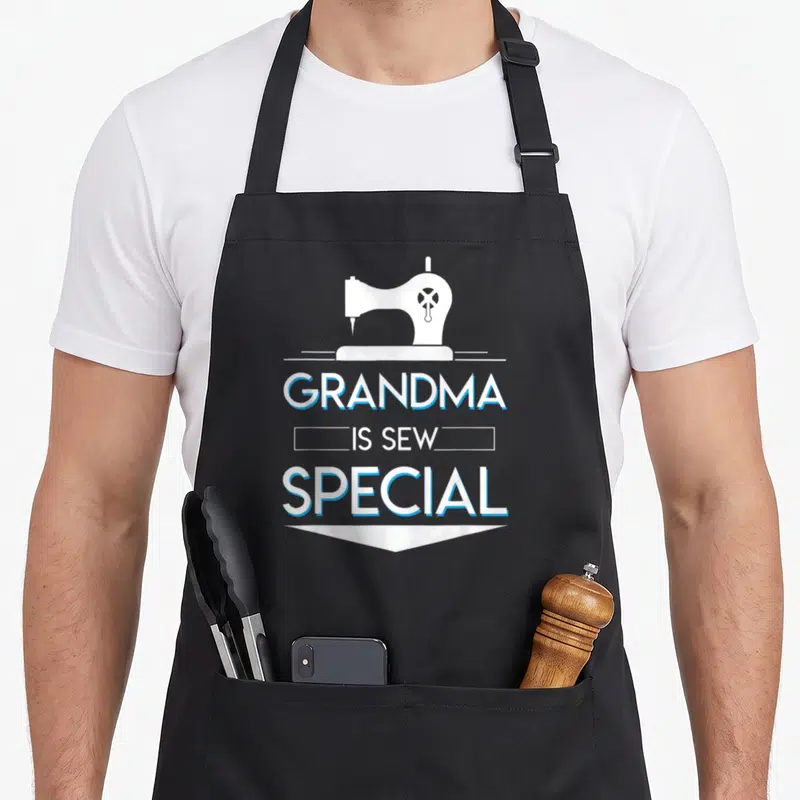 Sew grandma apron - White sewing machine above stacked text Grandma Is Sew Special with blue outlines — shown on a black cotton canvas apron against a white background