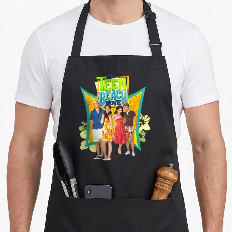 Channel beach apron - Stacked Teen Beach Movie title above four people in front of yellow and teal geometric shapes — shown on a black cotton canvas apron against a white background