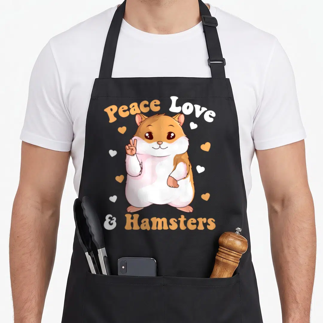 Peace lover hamster apron - Cartoon hamster with peace sign and hearts surrounded by orange and white text — shown on a black cotton canvas apron against a white background