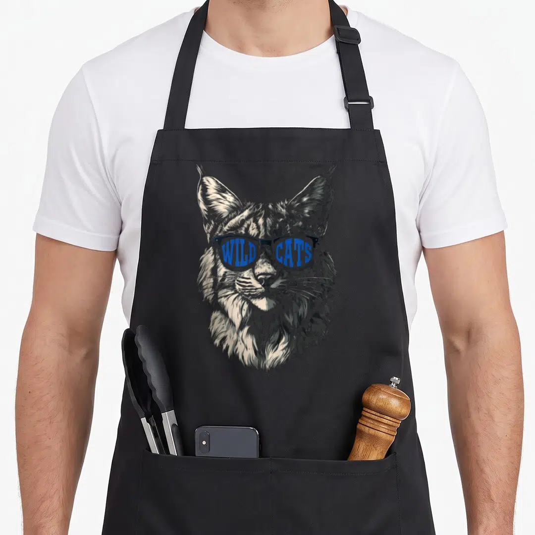 Wildcat cat apron - Lynx head line art wearing sunglasses with WILD CATS text in blue lenses — shown on a black cotton canvas apron against a white background