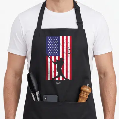 Vintage baseball american flag apron - Grey baseball batter silhouette over distressed red white and blue flag pattern — shown on a black cotton canvas apron against a white background