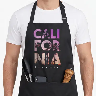 California tree apron - Split CALIFORNIA text filled with palm tree silhouettes and purple pink orange gradient sky — shown on a black cotton canvas apron against a white background