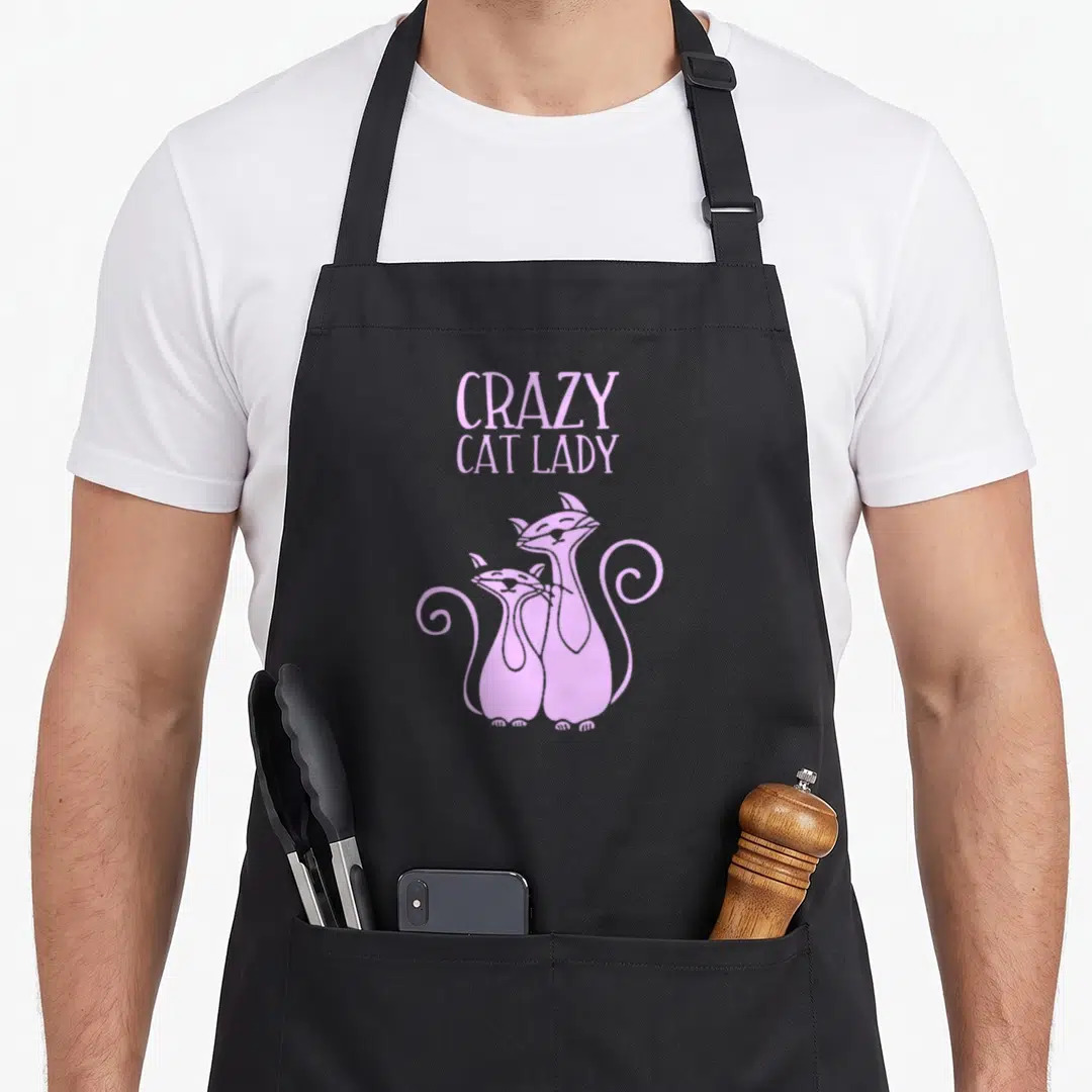 Vintage crazy cat lady apron - Two purple cartoon cats standing side-by-side below centered text reading CRAZY CAT LADY — shown on a black cotton canvas apron against a white background