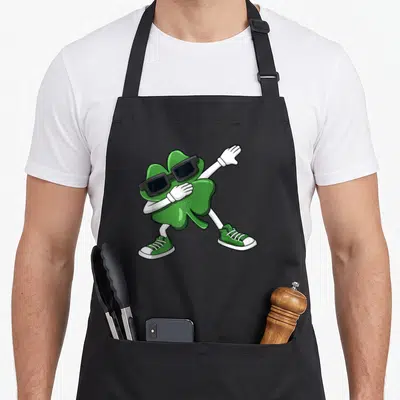 Dabbing shamrock st patrick day aprons - Cartoon green shamrock dabbing in black sunglasses and white gloves — shown on a black cotton canvas apron against a white background