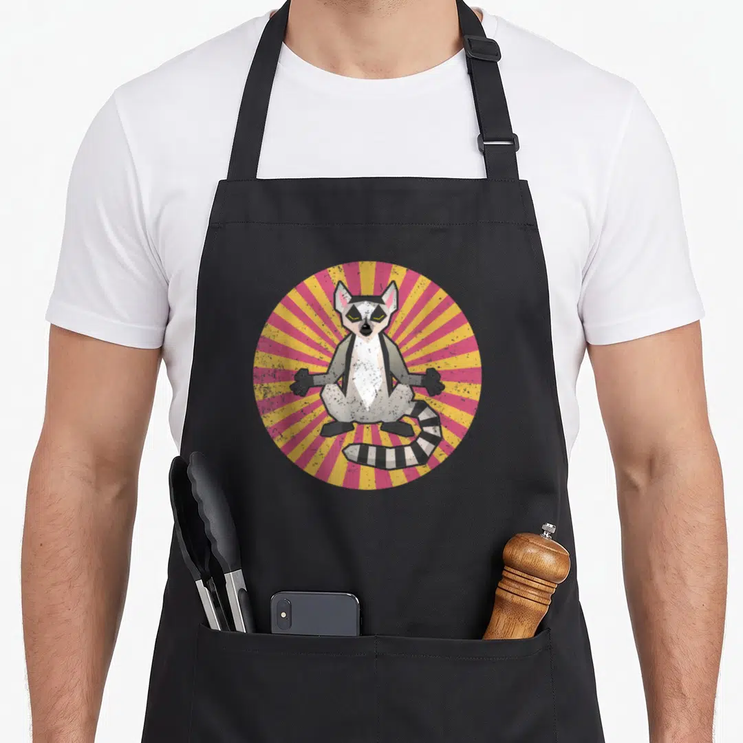 Funny lemur lover apron - Geometric lemur sitting in front of a pink and yellow sunburst circle — shown on a black cotton canvas apron against a white background