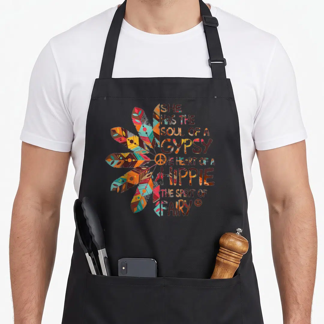 She hippie apron - Stacked text reading gypsy hippie fairy next to colorful feather cluster and peace symbols — shown on a black cotton canvas apron against a white background