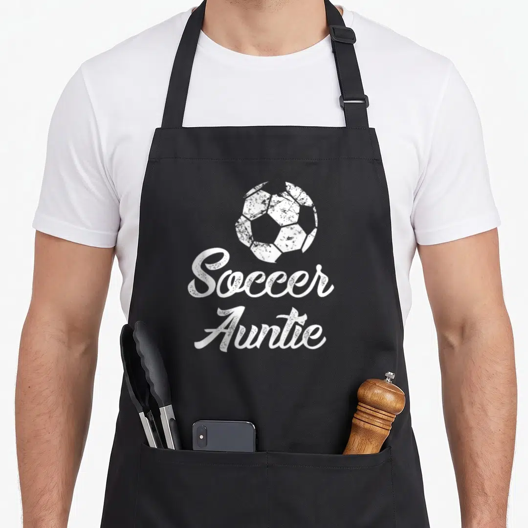 Soccer half player apron - White distressed soccer ball above script text reading Soccer Auntie — shown on a black cotton canvas apron against a white background