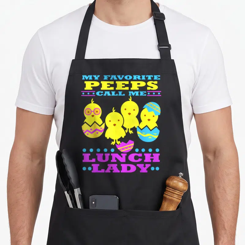 Easter cafeteria aprons - Four yellow chicks with eggshells and My Favorite Peeps Call Me Lunch Lady text in blue — shown on a black cotton canvas apron against a white background