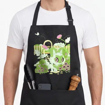 Sprigatito nature apron - Cartoon cat-like creature in a garden with pink flowers, fence, and flying butterfly in green — shown on a black cotton canvas apron against a white background