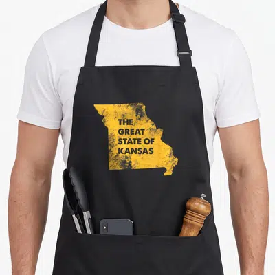 State kansas apron - Yellow Missouri map shape with grey text reading THE GREAT STATE OF KANSAS in distressed font — shown on a black cotton canvas apron against a white background