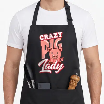 Pig animal farm apron - CRAZY PIG Lady text with pink cartoon pig illustration — shown on a black cotton canvas apron against a white background