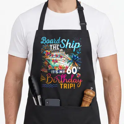 Board 60th birthday apron - Watercolor cruise ship with palm trees balloons and stacked text reading Board the Ship — shown on a black cotton canvas apron against a white background
