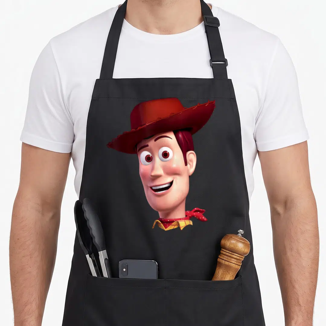 Woody face camping apron - Centered Woody head wearing red hat and bandana in brown and peach tones — shown on a black cotton canvas apron against a white background