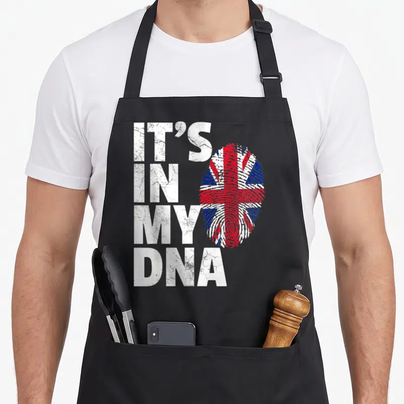 Britain union jack apron - Stacked IT'S IN MY DNA text beside a fingerprint filled with red white and blue Union Jack — shown on a black cotton canvas apron against a white background