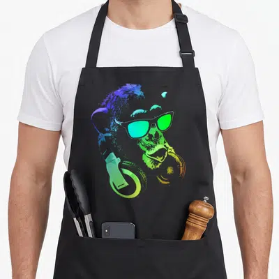 Chimp monkey apron - Rainbow splatter monkey head with sunglasses and headphones in blue green yellow orange purple — shown on a black cotton canvas apron against a white background